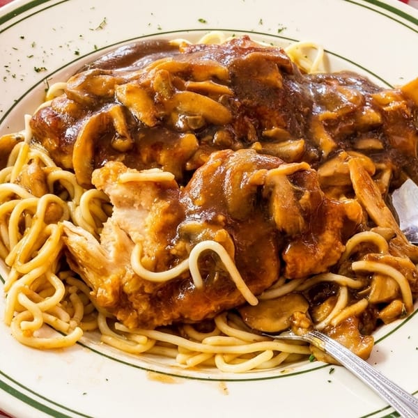 Chicken Marsala with mushrooms and spaghetti on a white plate with green stripes, on a red and white checkered tablecloth.