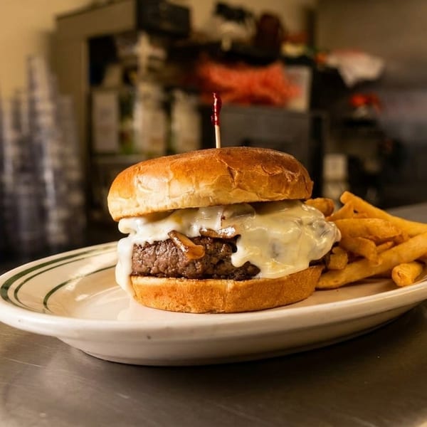Cheeseburger with melted cheese and caramelized onions, served with fries on a diner counter.